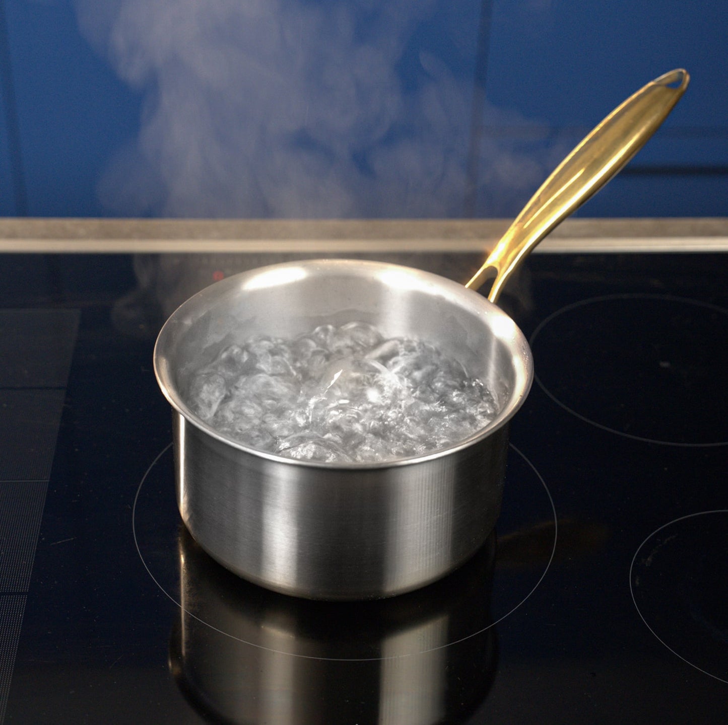 Titanium pot with boiling water on a black stovetop against a blue wall.