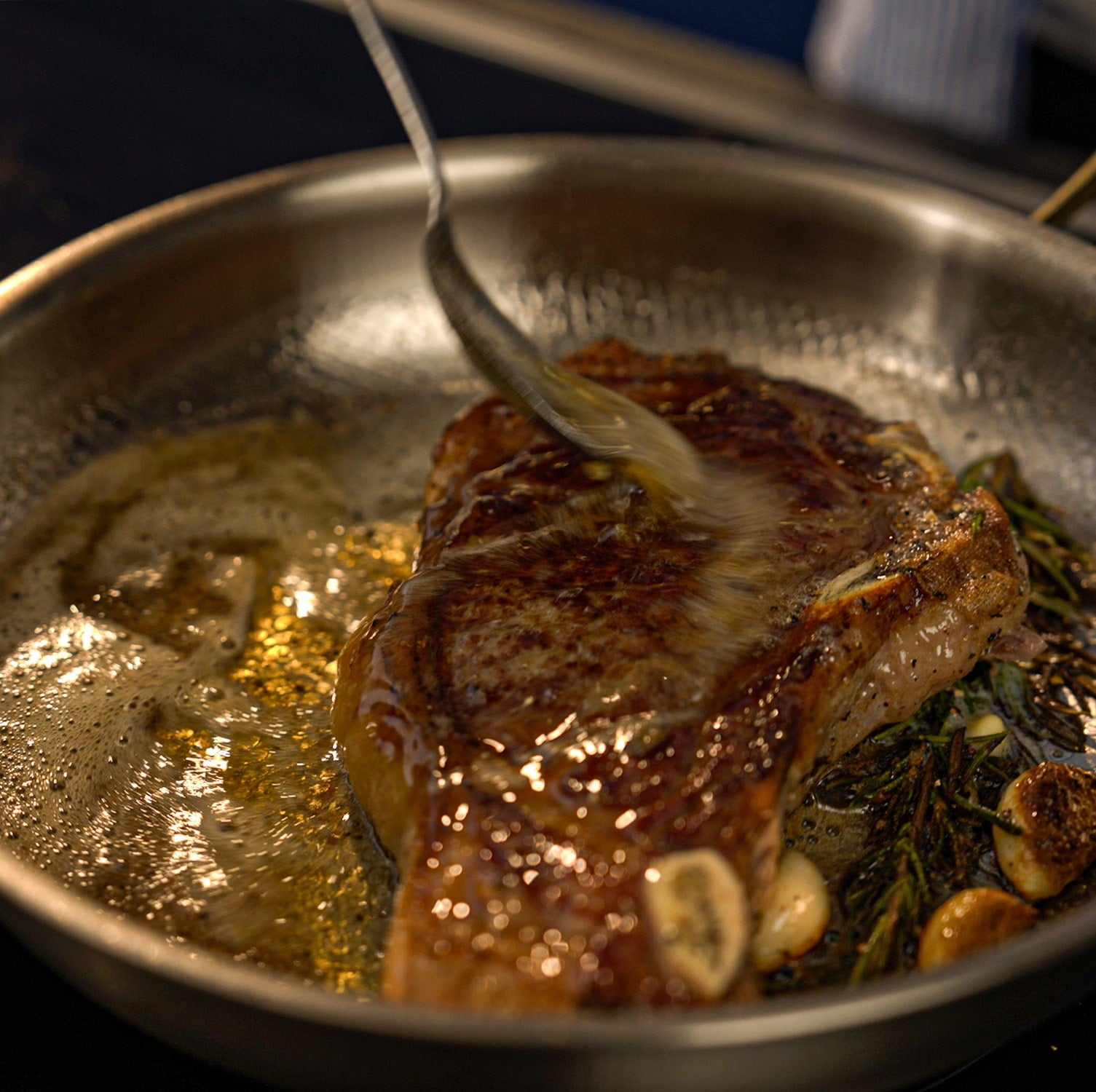Searing steak in a Titanium pan with herbs and garlic, close-up view.