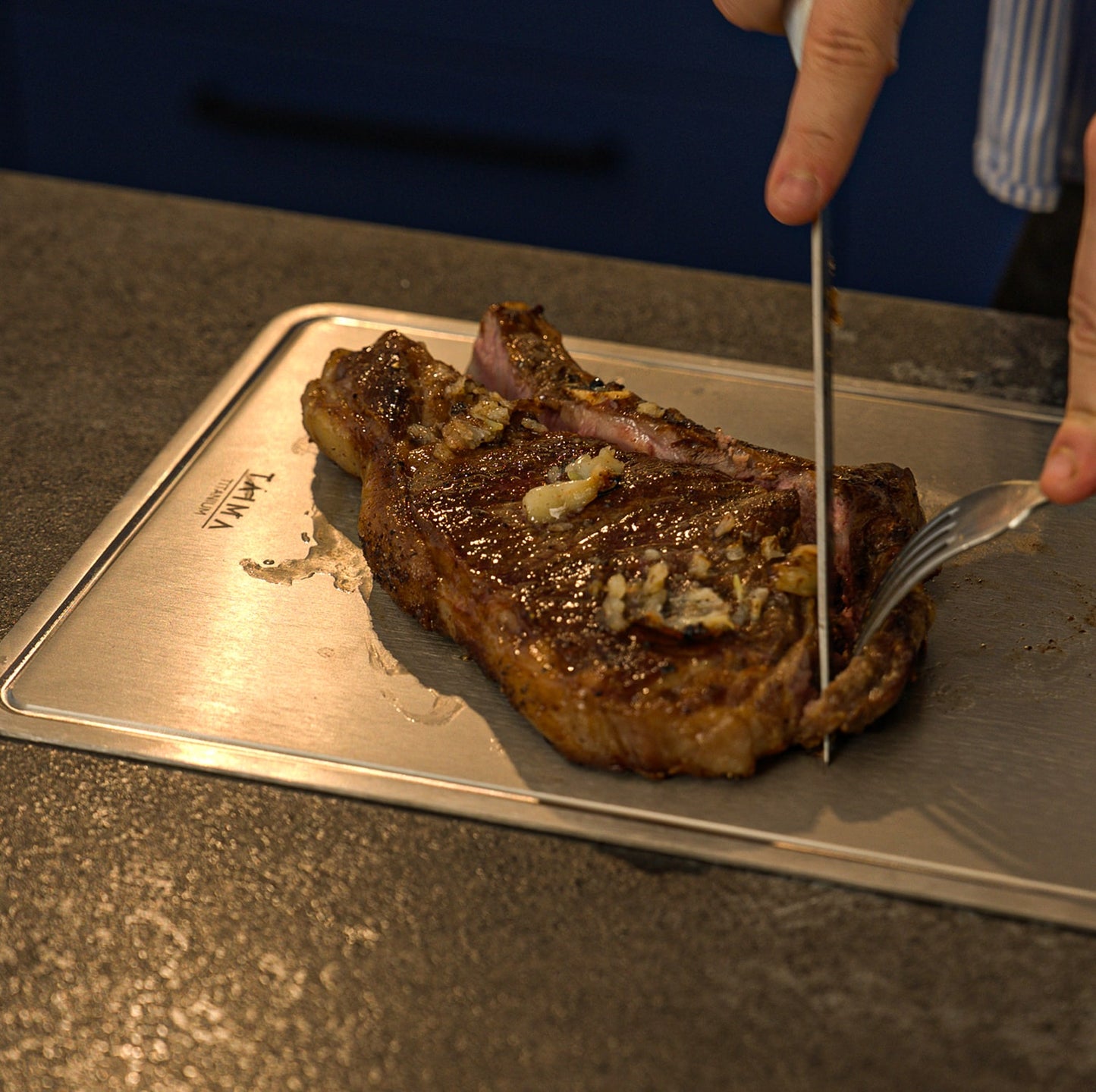 Steak being cut on a metal cutting board with a knife and fork.