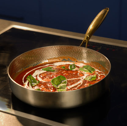 Titanium pan with tomato-based sauce and basil leaves on a stove