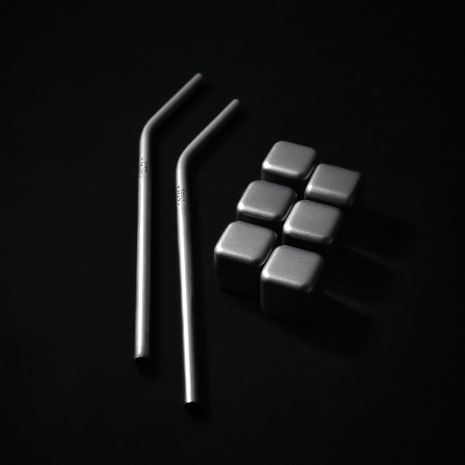 Two metal straws and six metallic dice cubes on a black background
