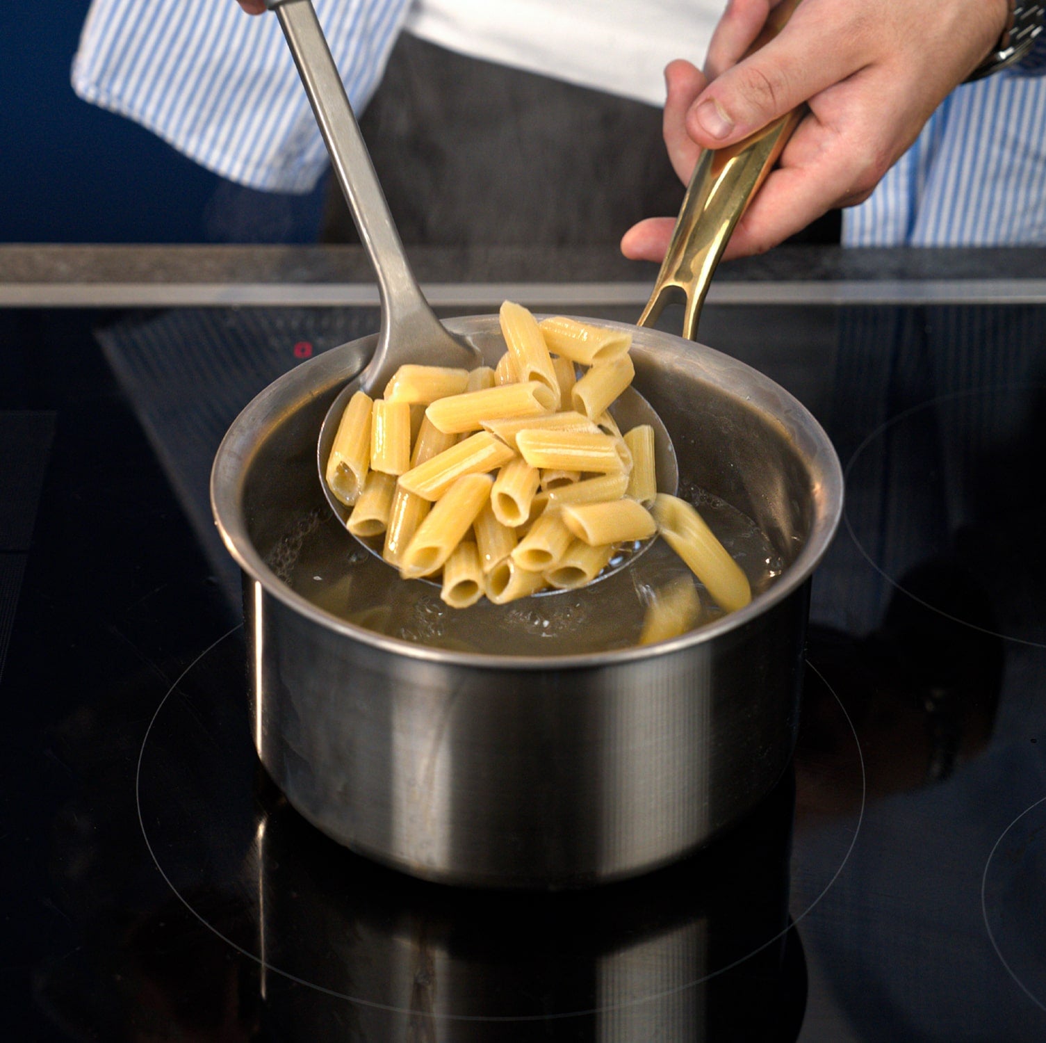 Pasta being served from a titanium pot with a ladle on a stove.