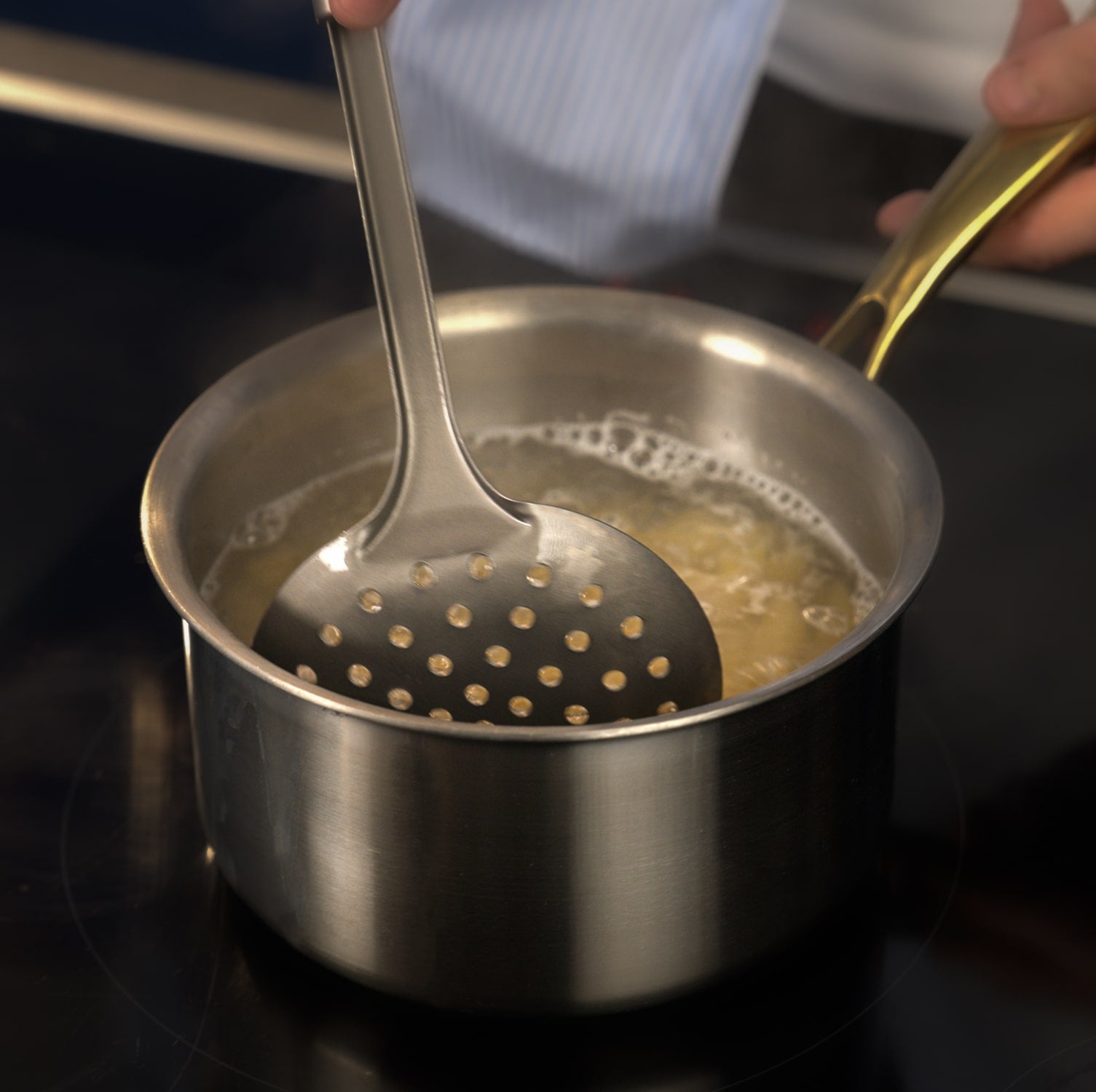 Stirring a pot of boiling liquid with a slotted spoon on a stove.