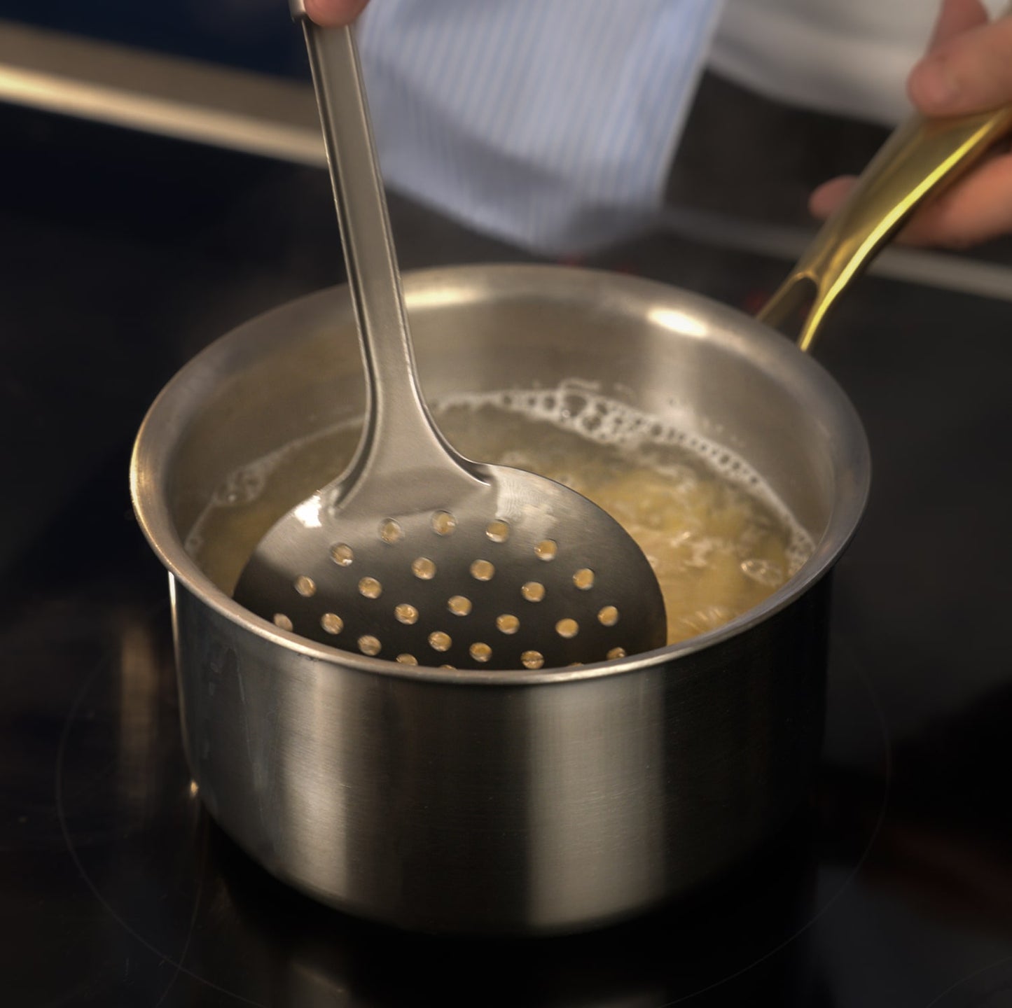 Stirring a pot of boiling liquid with a slotted spoon on a stove.