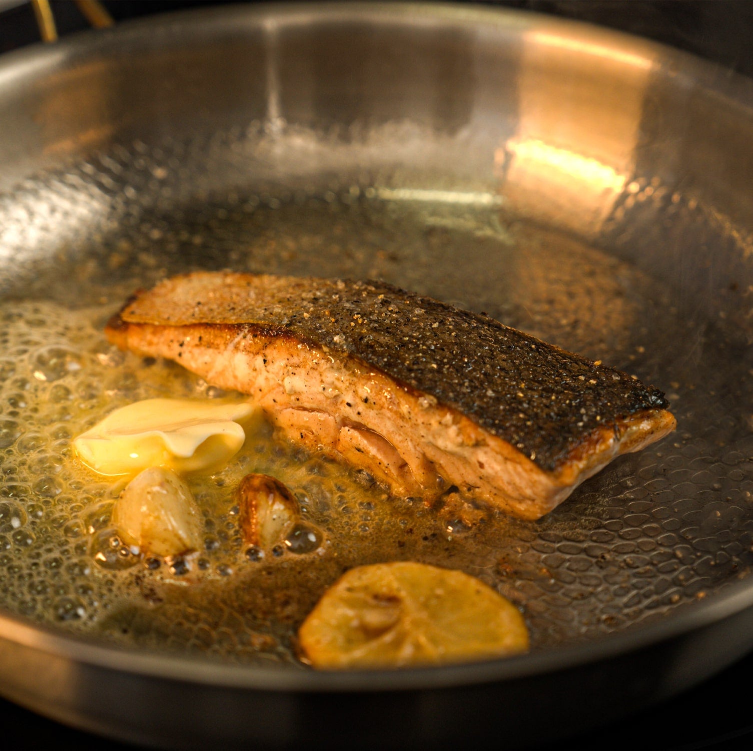 Salmon fillet cooking in a titanium pan with lemon slices.