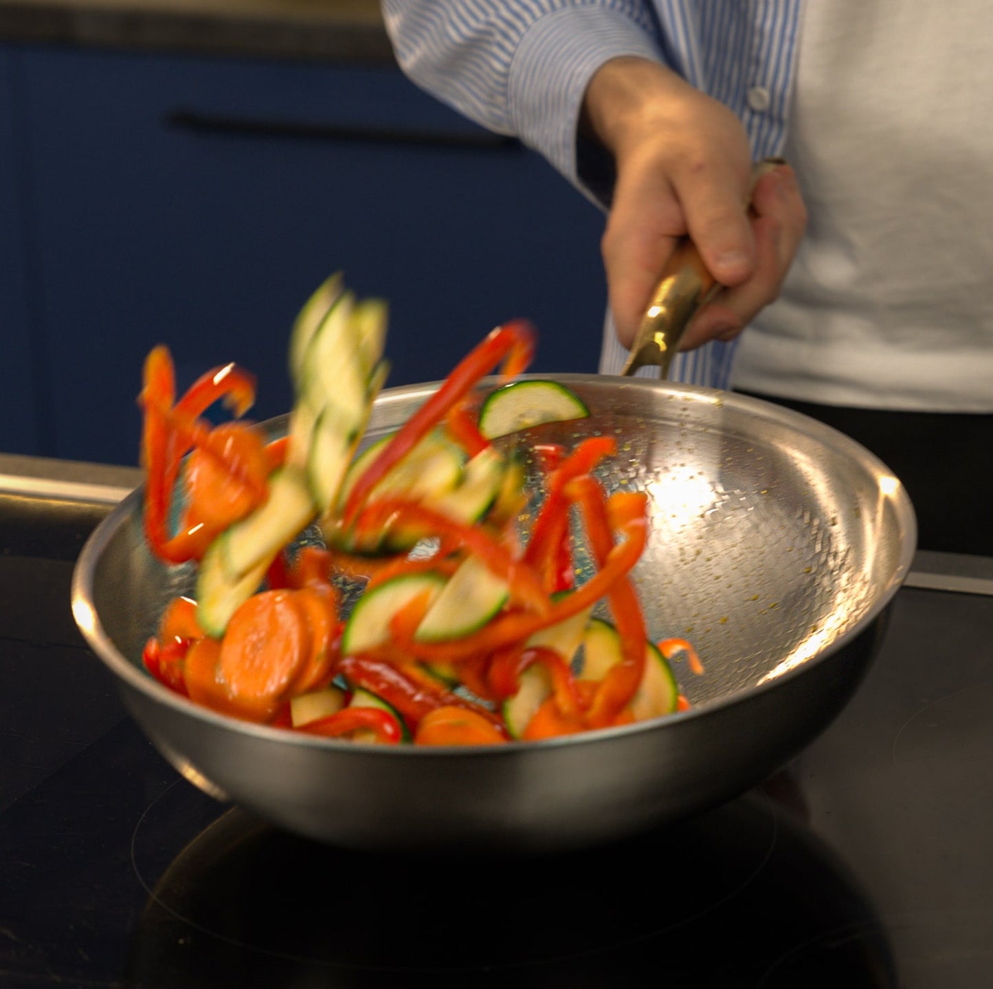 Person cooking sliced vegetables in a titanium pan on a stove